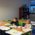 Творческие листы: двое детей выполняют разноцветные задания по русскому языку за столом.