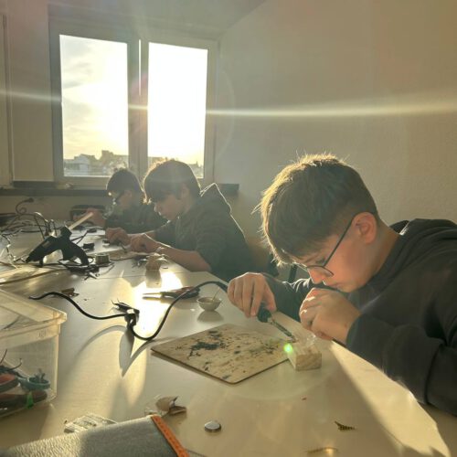 Jugendliche löten konzentriert an Projekten am langen Werktisch.